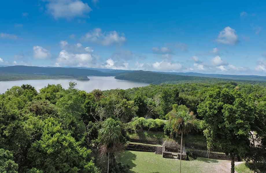 The serene Yaxha archaeological site with its ancient Mayan pyramids and structures overlooking the glistening Yaxha Lake in Guatemala.