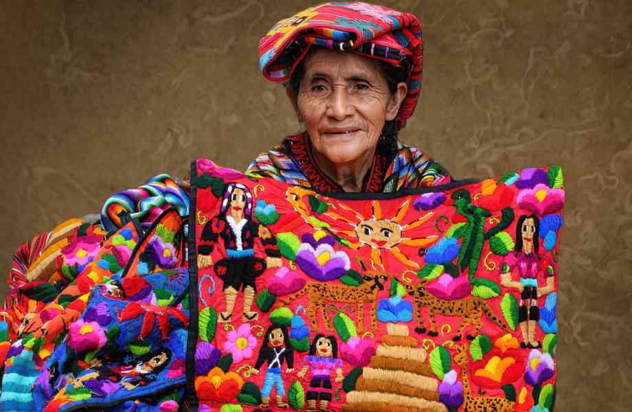 "Maya weaver showcasing vibrant textiles at Chichicastenango market - A colorful display of Guatemala's rich cultural heritage through traditional weaving artistry."