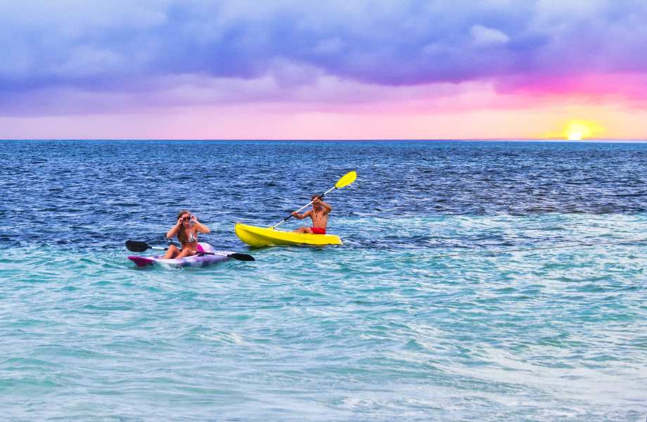 Adventurous couple kayaking at sunrise over the Caribbean waters in Belize, embracing the beauty of the moment.
