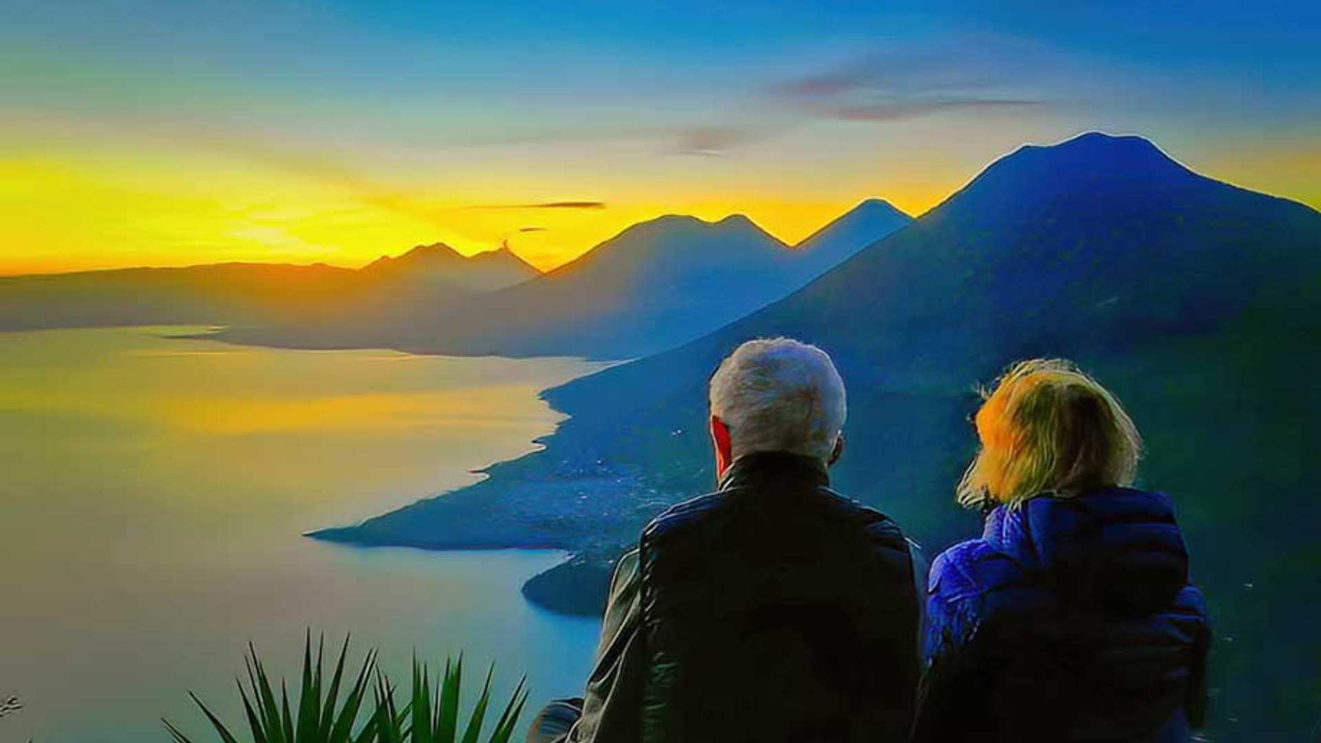 Couple admiring a serene sunrise over Lake Atitlan, with calm waters reflecting the morning sky.