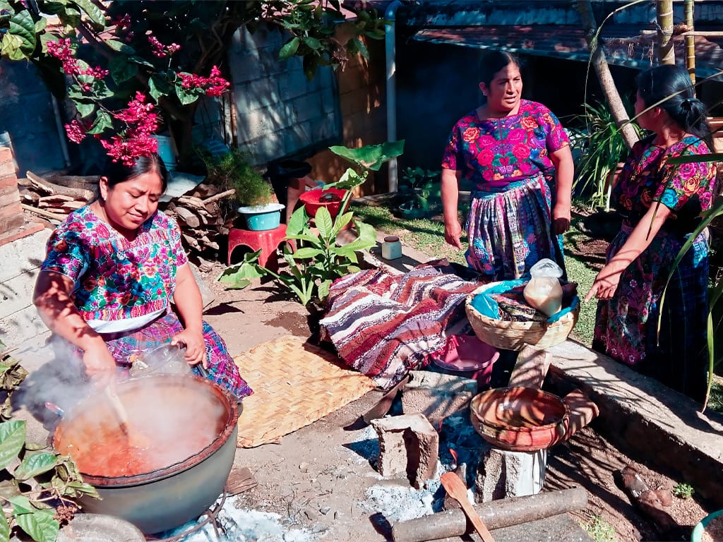 A group of Mayan women from Antigua, Guatemala, gathered around a traditional cooking station, sharing their culinary heritage and cultural traditions during a community-led tour with Martsam Travel.