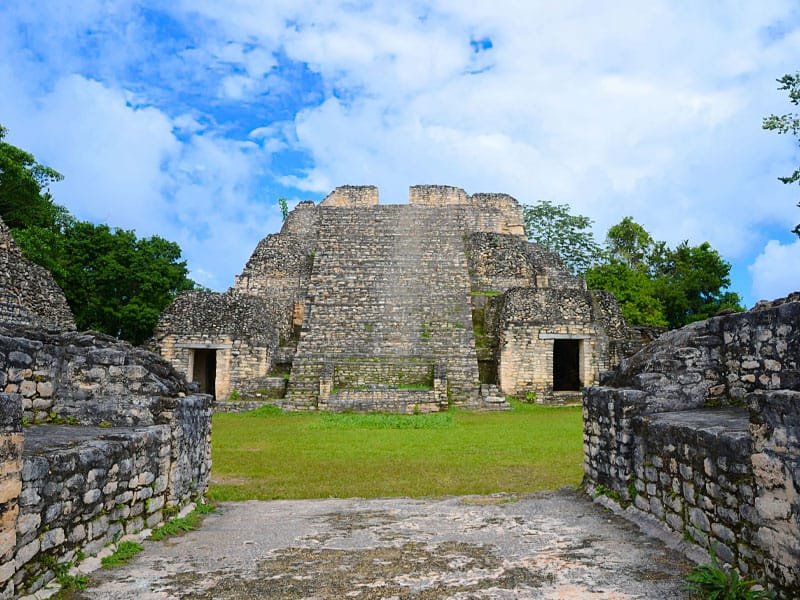 ncient Maya pyramid at Caracol archaeological site in Belize, surrounded by lush jungle and blue sky