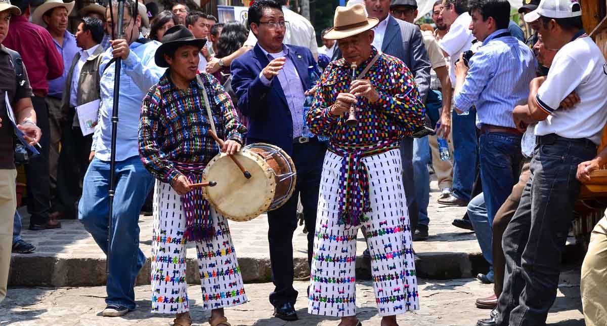 Maya musicians in traditional attire performing by Lake Atitlán, with vibrant instruments and cultural expression in a scenic lakeside setting.