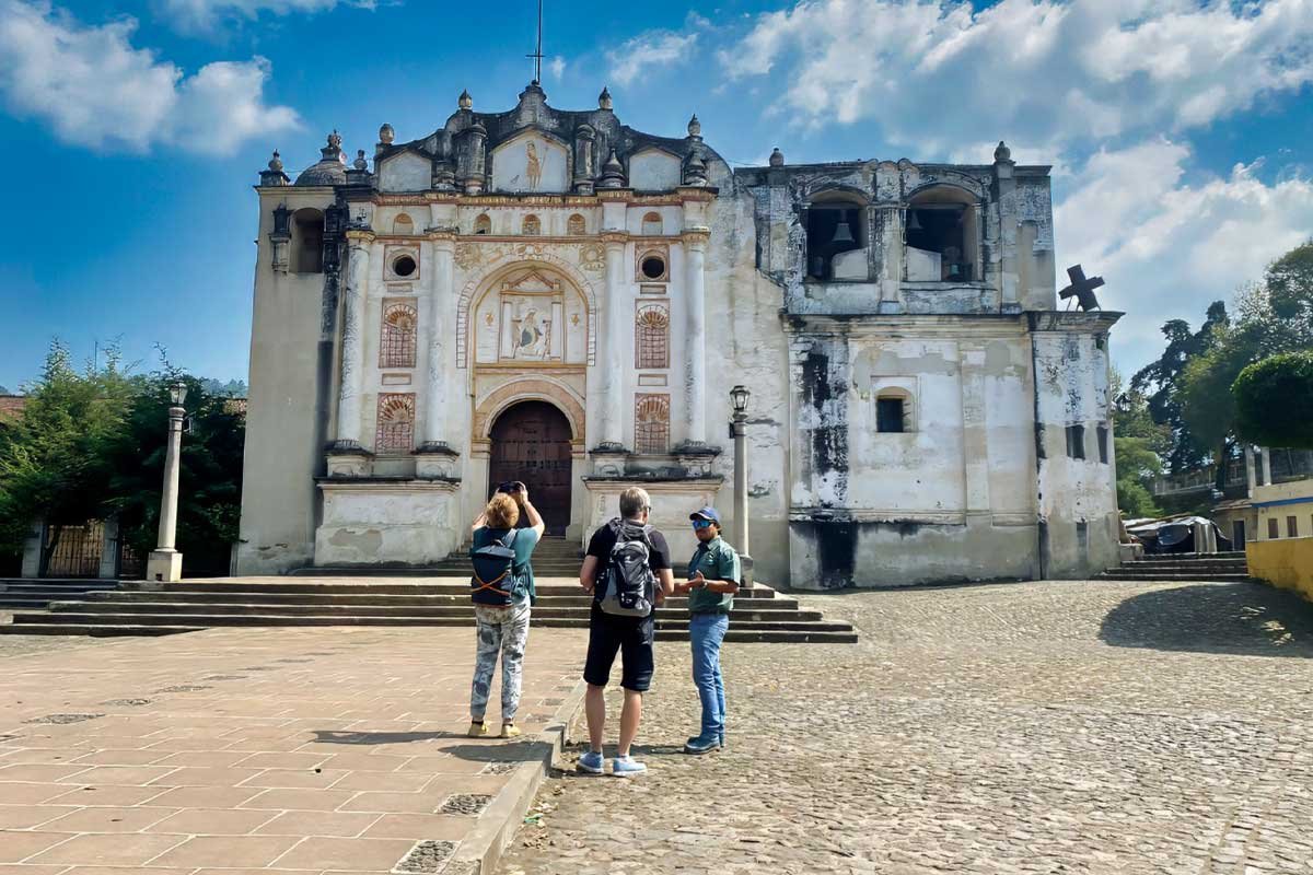 Tour guide explains the history of Antigua Guatemala to two visitors in front of a colonial UNESCO church, during one of our custom Central America tours.