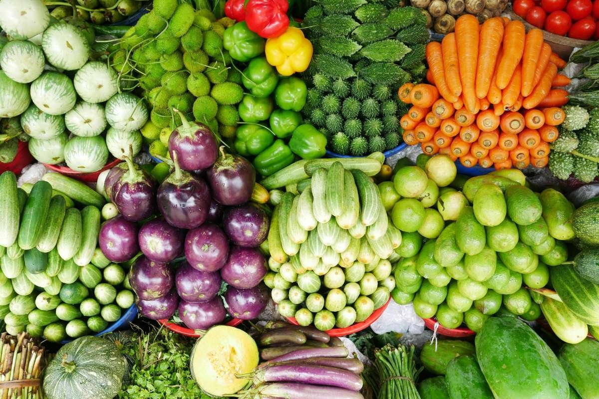 Colorful display of fresh vegetables used in traditional Guatemalan cuisine, including tomatoes, peppers, corn, and herbs at a local market