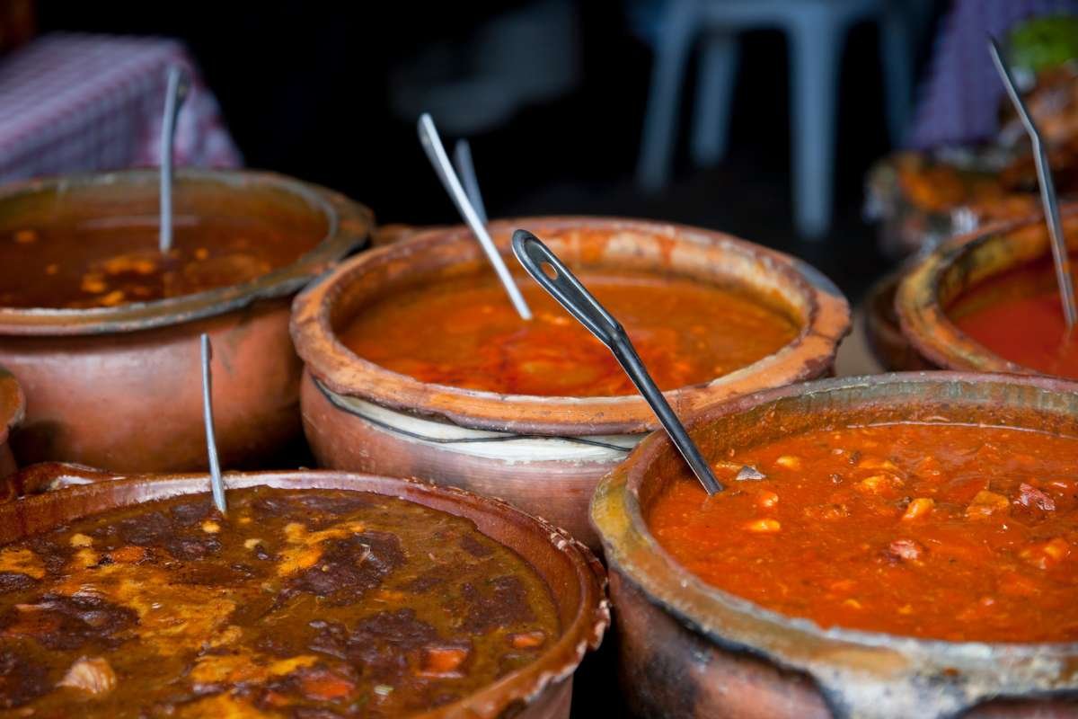 Traditional Guatemalan cuisine served in a rustic ceramic pot, featuring Pepián, and a vibrant display of authentic Guatemalan dishes