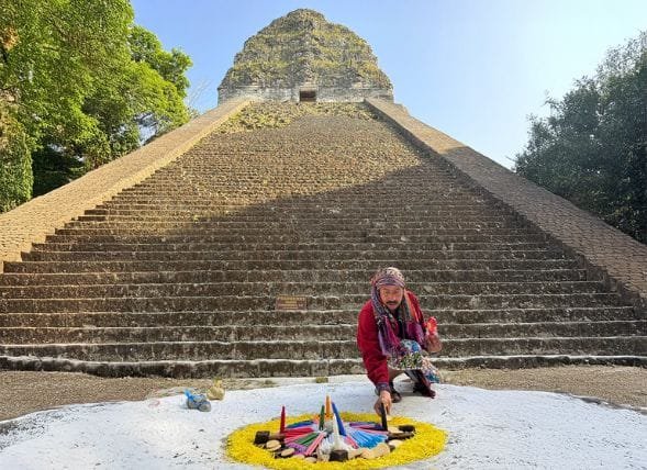 Traditional Mayan shaman performing a ceremony at his altar in front of Tikal Temple V, featured in our immersive luxury Guatemala vacation packages.