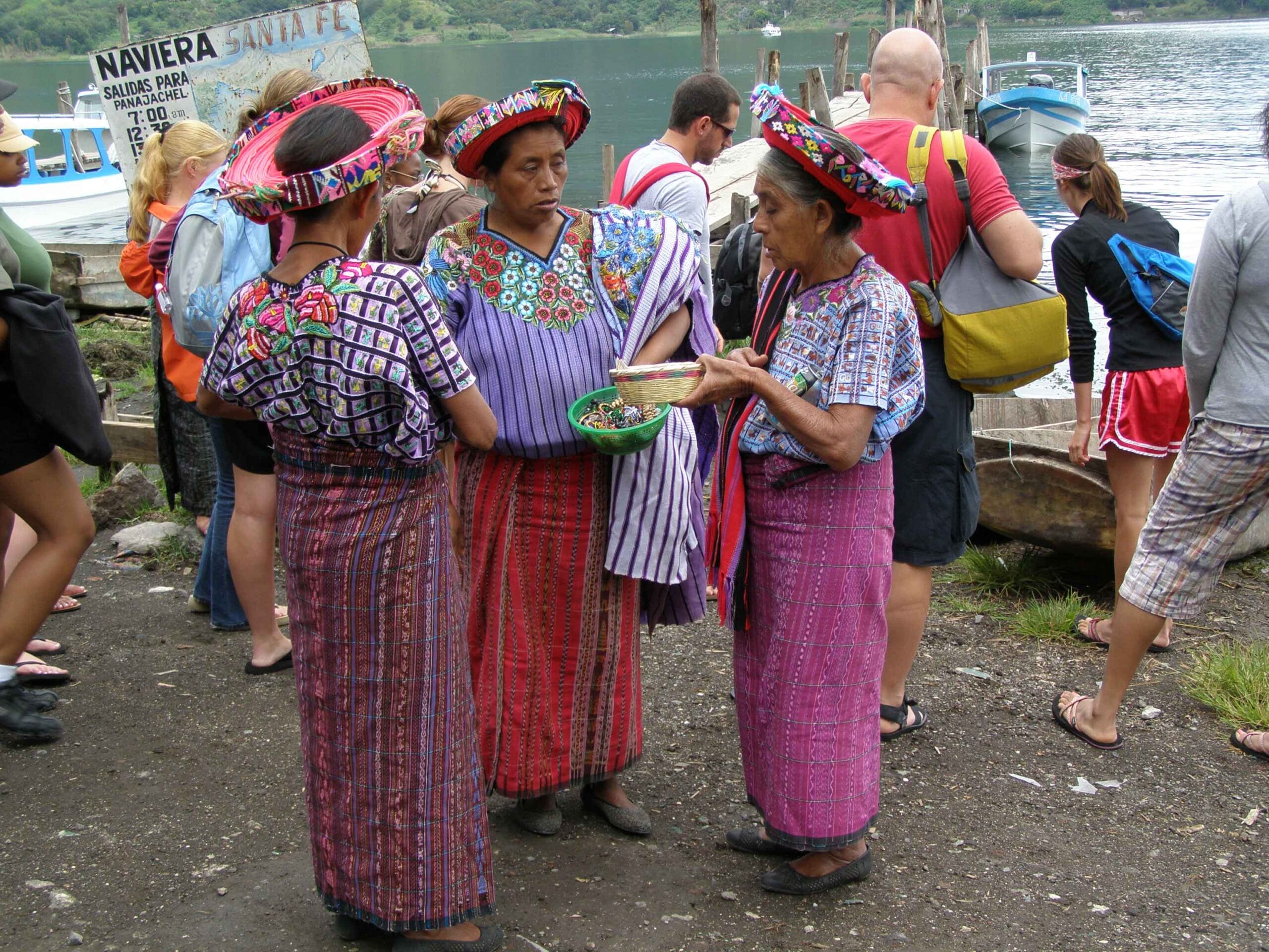 Guatemala cultural tours image of three women from Lake Atitlán wearing traditional clothing and tocoyales, talking on the beach