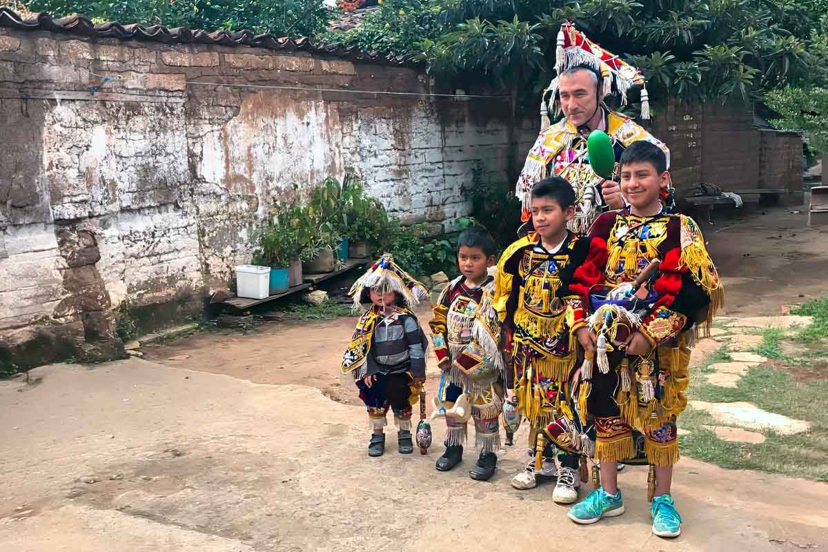 Private indigenous tours in Guatemala showing a visitor wearing traditional dance attire sharing a joyful moment with local child dancers during a cultural immersion experience
