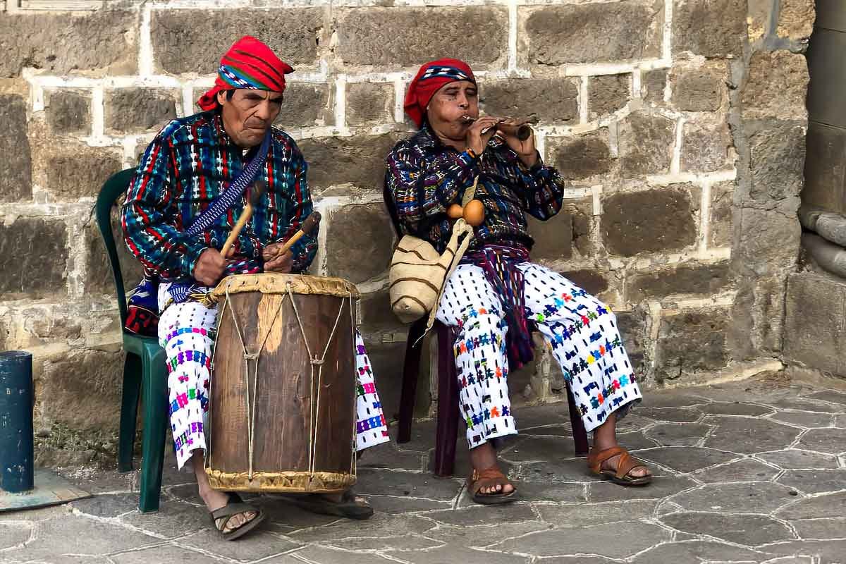 Private indigenous tours in Guatemala featuring a Maya musician playing traditional music in front of a church in San Juan La Laguna, Lake Atitlán