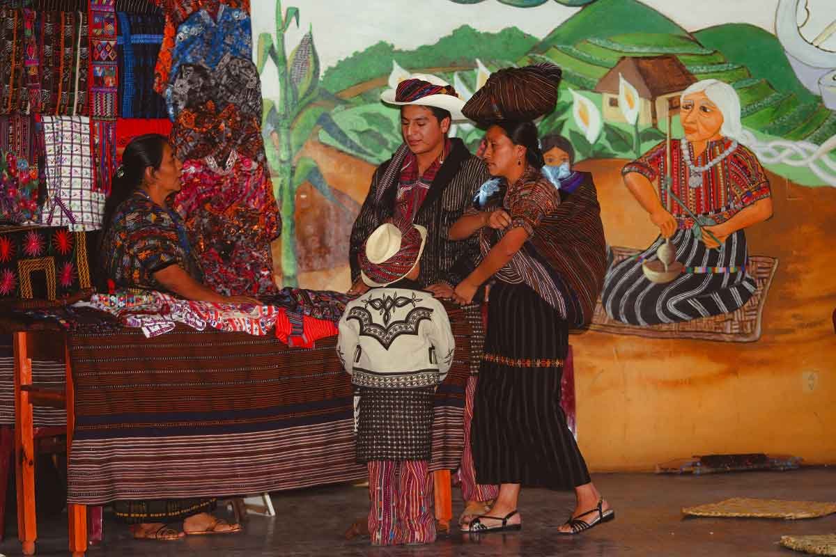 Private indigenous tours in Guatemala showing a local family buying textiles from a vendor in Sololá, wearing traditional Maya clothing 