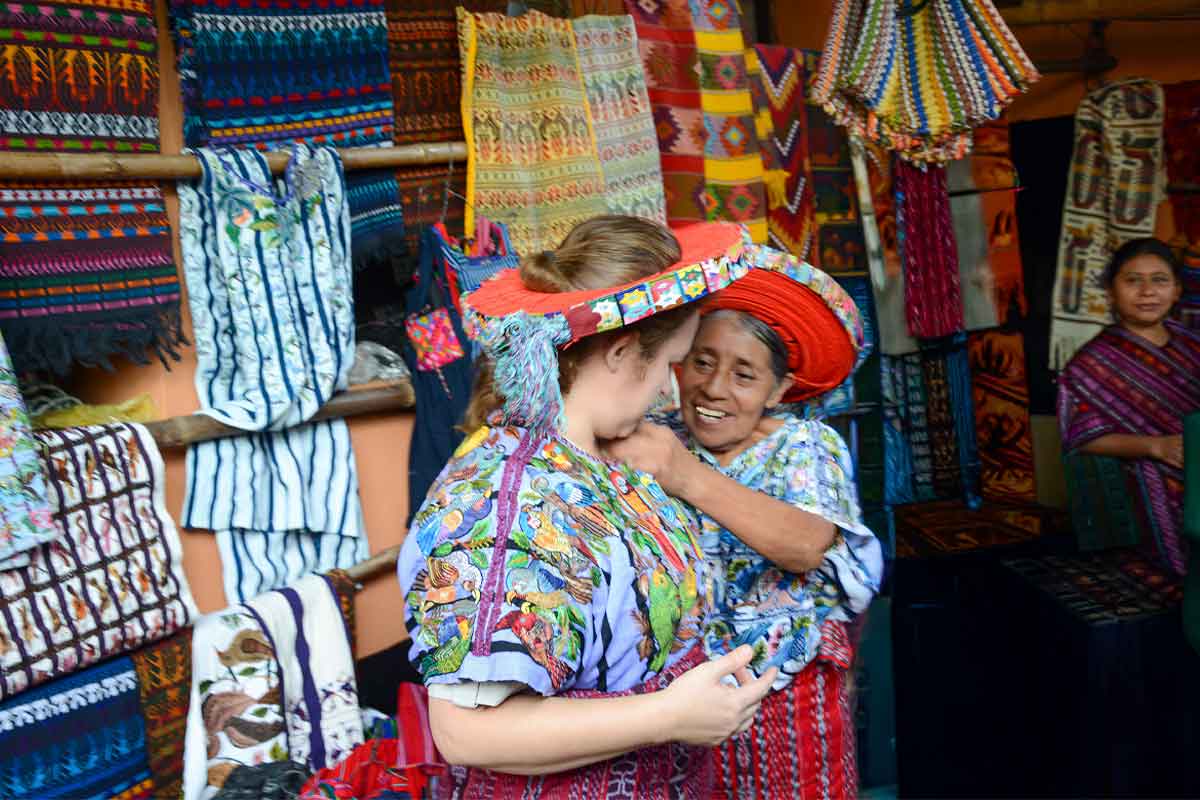 Traveler being helped by an elder Maya woman while trying traditional colorful clothing in a lakeside community during private cultural tours Guatemala experiences