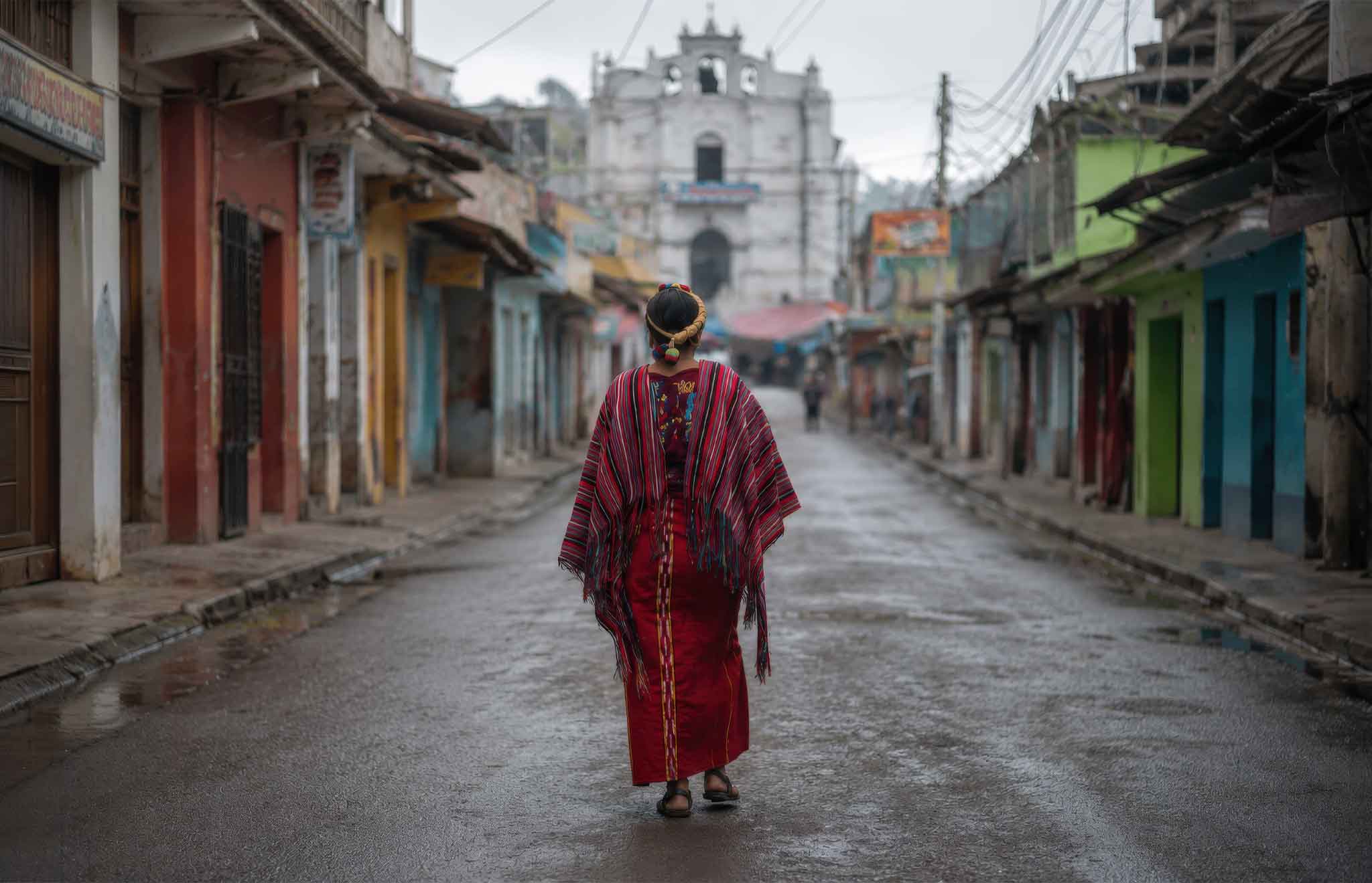 Maya woman wearing traditional Maya clothing Guatemala while walking through the streets of Chajul, with the community church visible in the background of the Ixil Highlands.