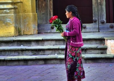 Woman in traditional embroidered clothing carrying red roses in San Cristóbal de las Casas during a Chiapas Cultural Tour.