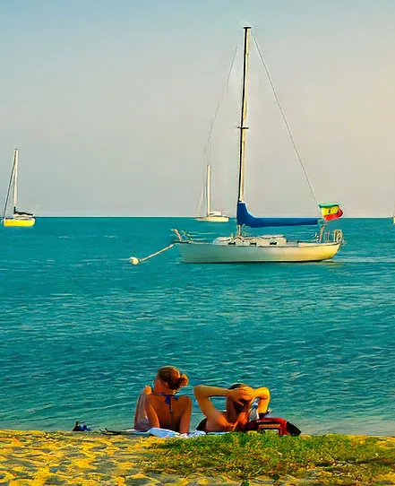 Two travelers relaxing beside turquoise coastal water with sailboats offshore in Belize.