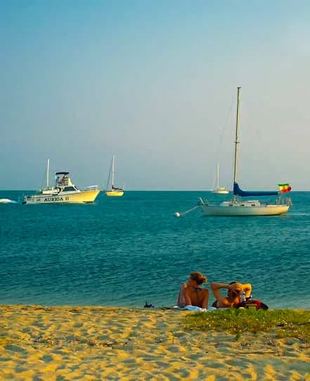 Couple-caribbean-beach-belize | martsam travel Couple relaxing on a Caribbean beach in Belize with sailboats anchored offshore.
