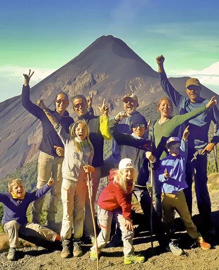 Adults and children posing together on a hike with a volcano behind them in Guatemala.