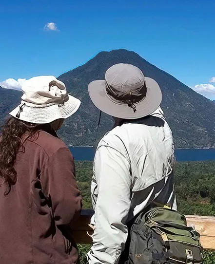 A couple standing at a lakeside viewpoint above Lake Atitlán and its surrounding volcanoes.