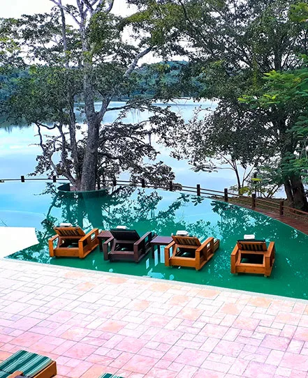 Pool with submerged lounge chairs overlooking a lake surrounded by trees.