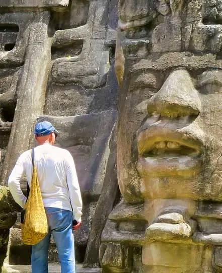 Lamanai-mask-temple-belize | martsam travel Traveler standing beside a monumental Maya mask at the Lamanai archaeological site in Belize.