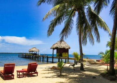 Palm-lined beach with a hammock and waterfront pier in Placencia, Belize
