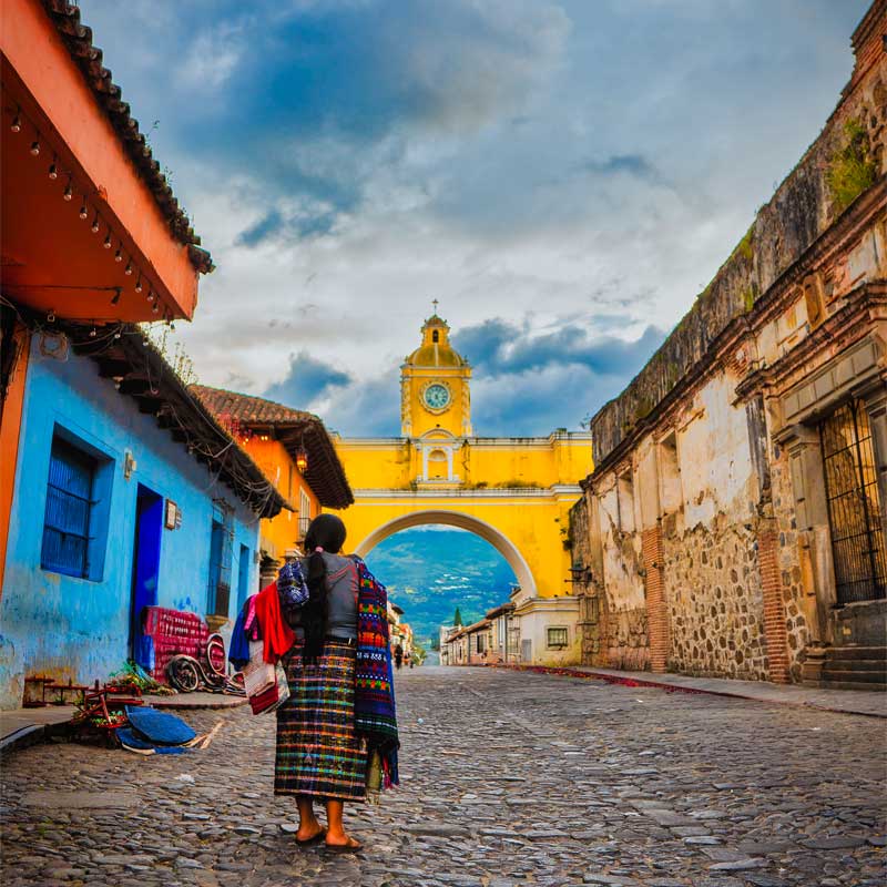 Guatemala Tour Packages with a Maya woman walking toward Santa Catalina Arch in Antigua Guatemala